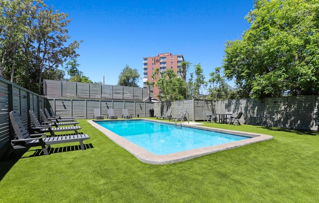 a backyard with a pool and lounge chairs in front of a fence