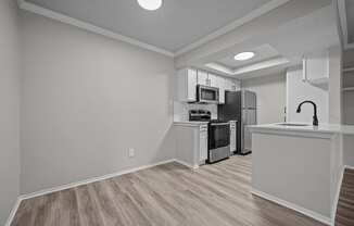 the kitchen and living room of an apartment with white walls and wood flooring