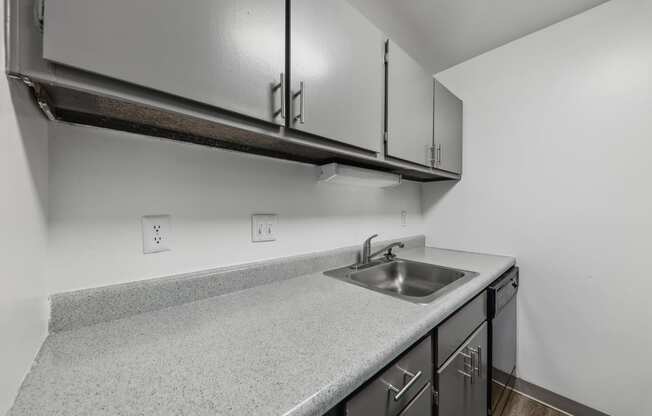 an empty kitchen with white countertops and a stainless steel sink