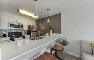 Kitchen Bar Seating with White Countertop, Mugs and Bowls, Sink and "A Man Walks Into a Bar" Painted on the Wall, 