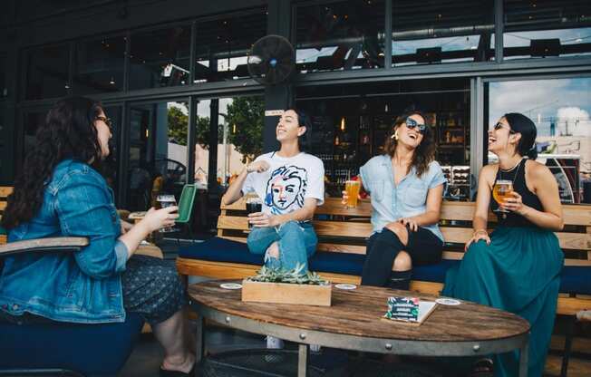 a group of women sitting around a table drinking beer