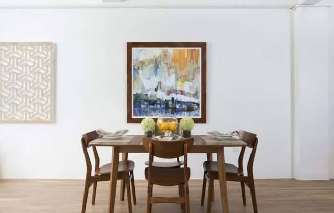 A brown wooden dining table with four chairs and a painting on the wall.
