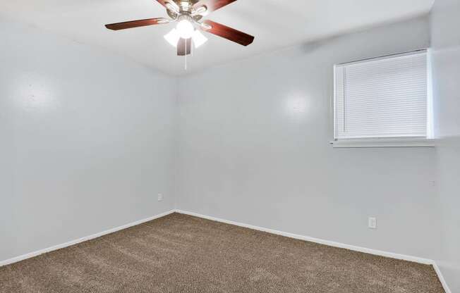 large carpeted room with ceiling fan and window