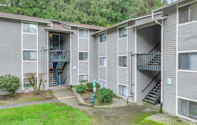 A grey apartment building with a small garden in front.