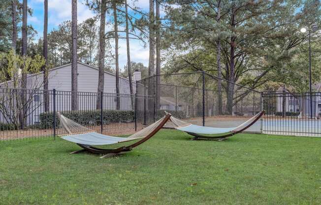two hammocks in the grass in front of a fence