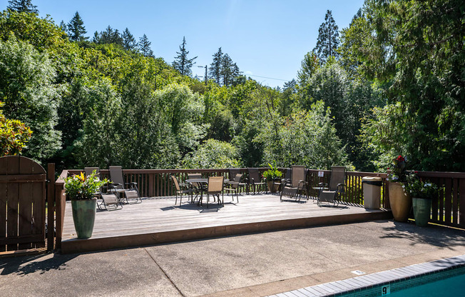 A pool area with chairs and a table surrounded by trees.