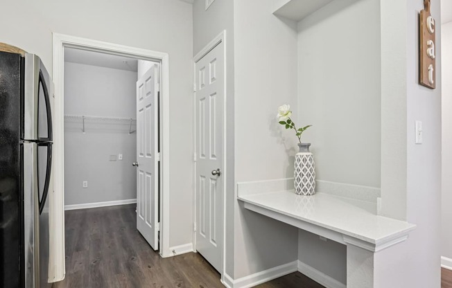 A kitchen with a refrigerator, a bench, and a doorway leading to another room.