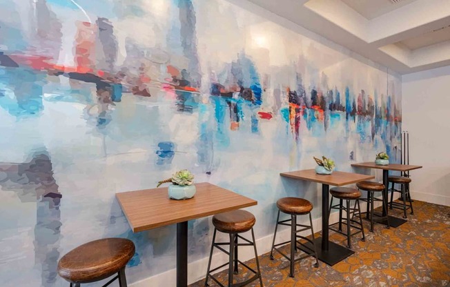 a room with a large painting on the wall and wooden tables and stools in front of