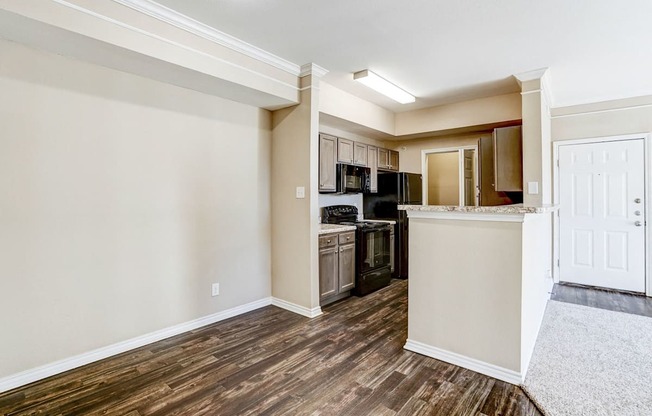 Open kitchen at Saxony at Chase Oaks Apartments in Dallas, TX, with wood-style flooring, dark cabinetry, black appliances, and a breakfast bar.