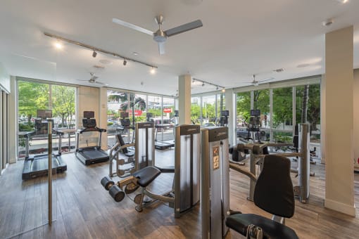 a gym with cardio machines and other exercise equipment in a building with large windows