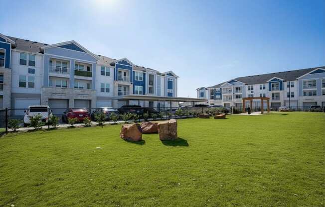 A sunny day at a grassy field with apartment buildings in the background.