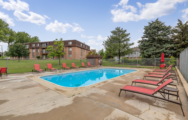 A pool surrounded by red chairs and trees.