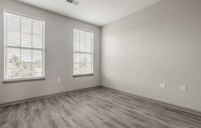 an empty room with wood flooring and two windows