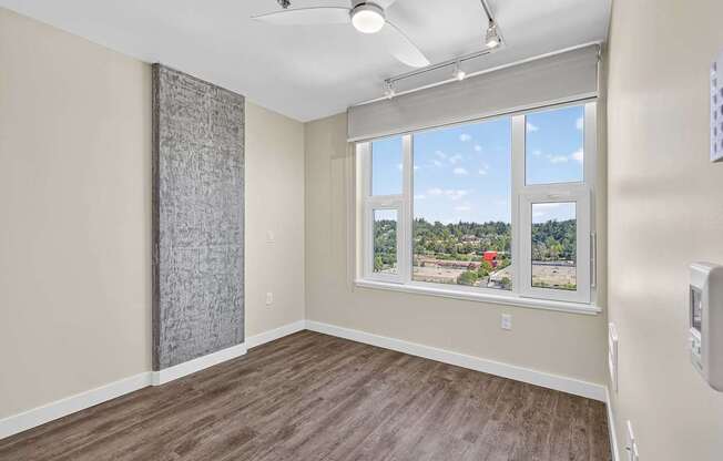 A room with a window that has a view of a red building and trees outside.