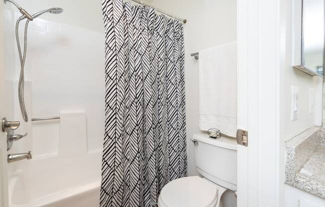 A white toilet sits under a shower curtain in a bathroom.