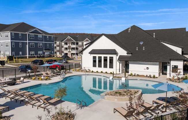 A large swimming pool surrounded by lounge chairs and umbrellas in front of a building.