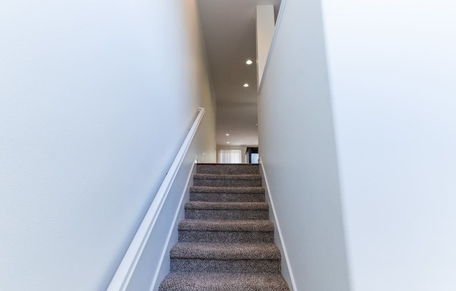 a view down the stairs of a hallway with carpeted stairs and white walls at The Vines at Riverpark, LLC, California, 93036