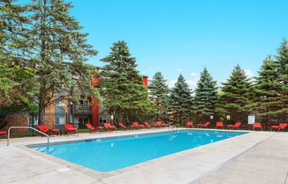 a swimming pool with red chairs around it in front of a building