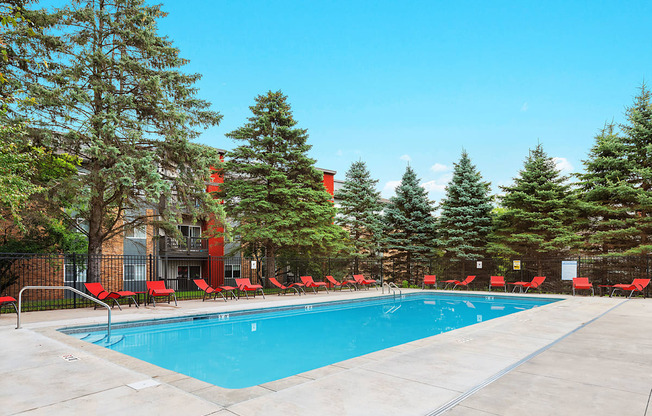 a swimming pool with red chairs around it in front of a building