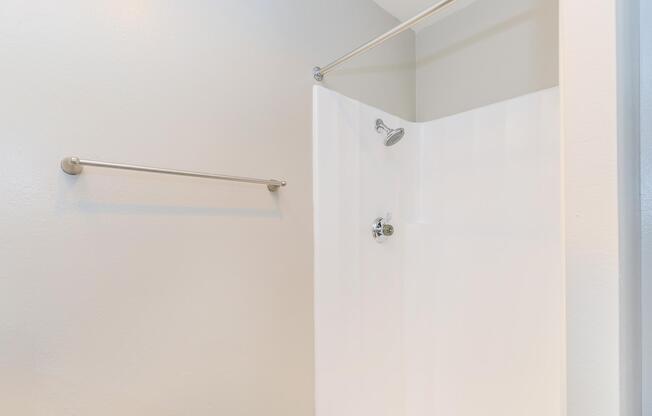 A clean, modern shower with a white acrylic enclosure and a ceiling-mounted showerhead. The walls are painted in a light color, providing a fresh and minimalistic appearance. A towel bar is mounted on the wall outside the shower area.