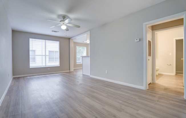 A room with a ceiling fan and light, hardwood floors, and a window with blinds.
