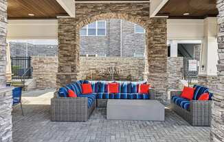 A patio with a grey wicker couch and a stone wall.