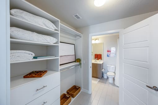 a closet with white shelves and pillows and a bathroom with a toilet