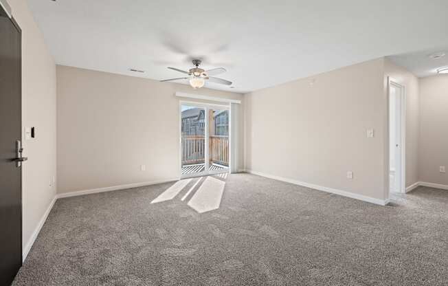 Spacious living room with ceiling fan and sliding door leading to a private balcony at Olde English Village