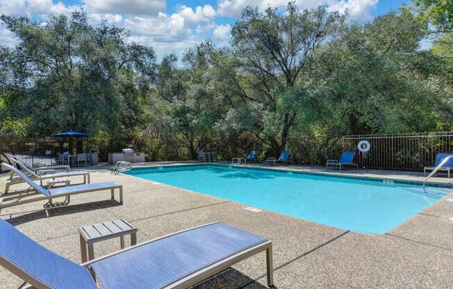 One of several swimming pools on-site.  This one is surrounded by oak trees in the distance.  Deck has lounge chairs and tables. 
