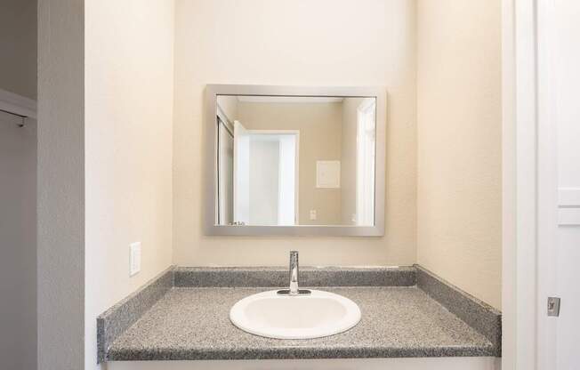 A bathroom sink with a granite counter top and a mirror above it.