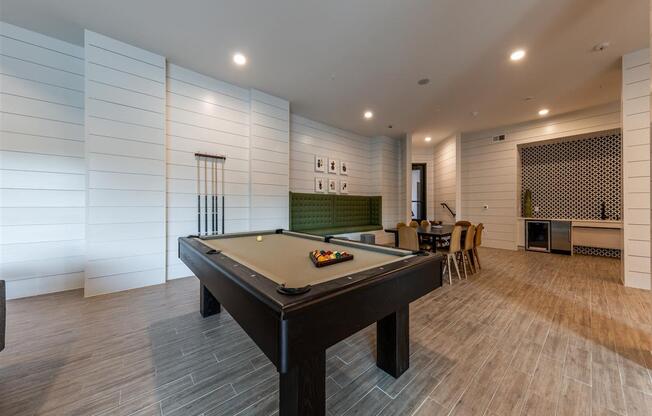 A billiards table near a seating area with a table, 8 chairs, and a wet bar in a clubhouse.