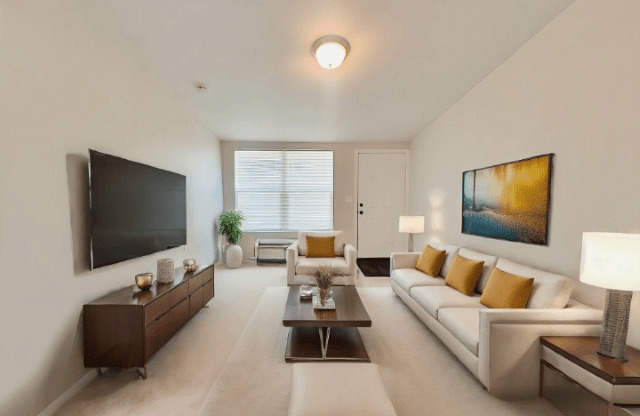 A modern living room with a white sofa, a wooden coffee table, and a large painting on the wall.