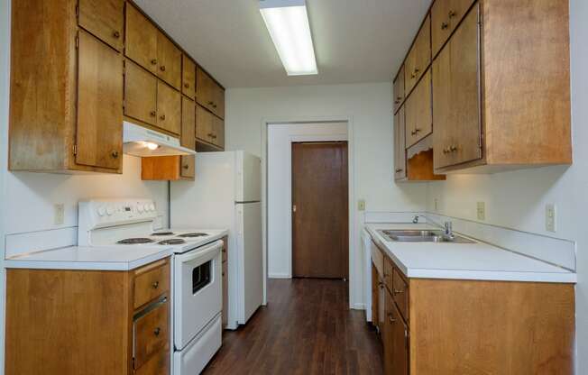 an empty kitchen with white appliances and wooden cabinets. Fargo, ND Country Club Apartments.