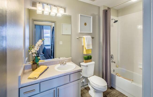 Bathroom with tub/shower, toilet, and sink with extended counter, wood designed flooring and high ceiling at Evergreens at Mahan apartments in Tallahassee, FL