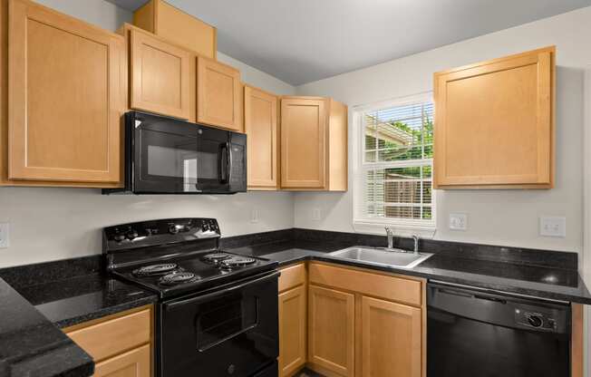 a kitchen with black counters and black appliances and wooden cabinets