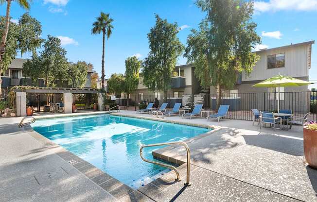 A pool surrounded by chairs and trees.