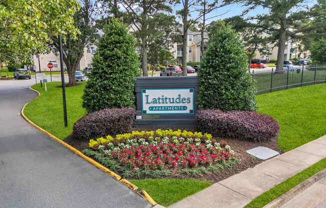 A sign for Latitudes Capayment surrounded by greenery and flowers.