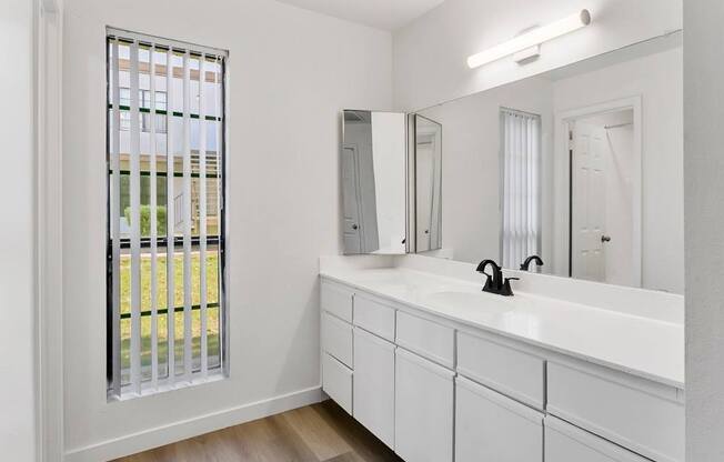 A white bathroom with a window and a sink.