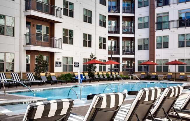 a swimming pool with lounge chairs and umbrellas in front of a building