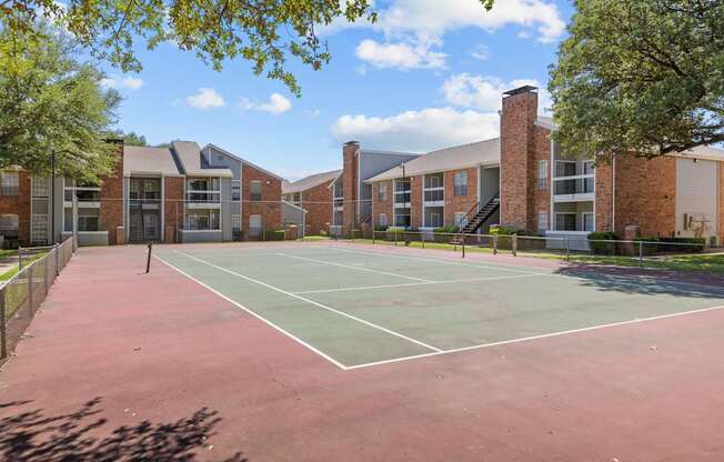A tennis court is surrounded by a brick building.
