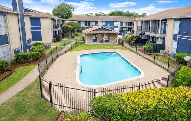 A small pool surrounded by a black fence and green bushes.