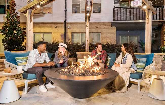 A group of people are sitting around a fire pit on a patio.