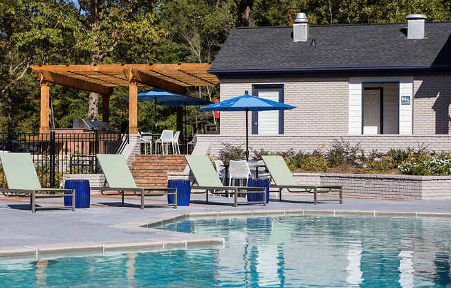 a swimming pool with chairs and umbrellas next to a house