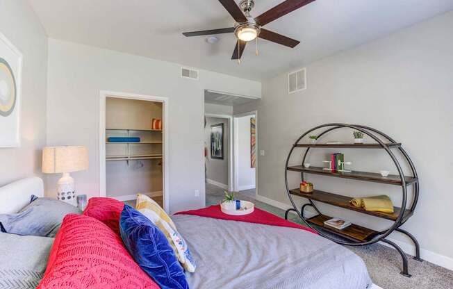 A bedroom with a bed, a ceiling fan, and a shelf.