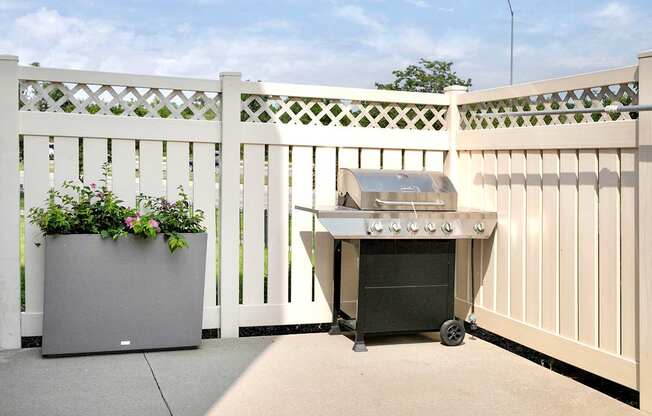 a patio with a grill and a white fence