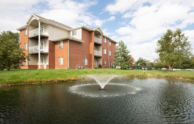 a fountain in the middle of a pond in front of an apartment building