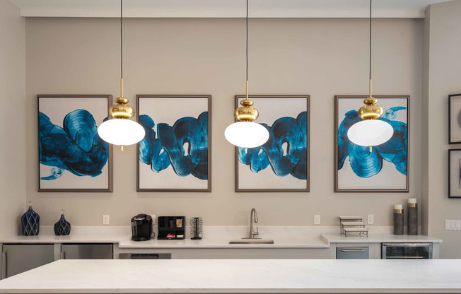 Three blue and white paintings hang on a wall above a kitchen counter.