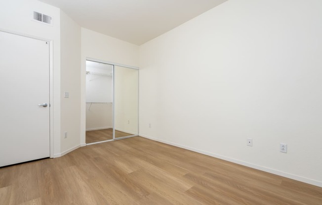 a bedroom with white walls and wood flooring and a closet