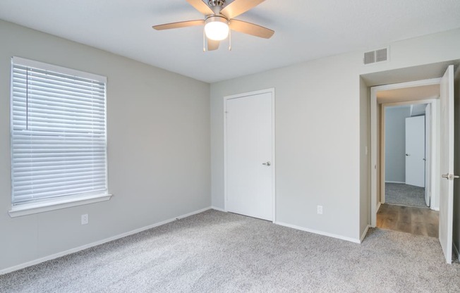 an empty bedroom with a ceiling fan and a door to a hallway