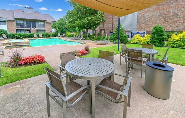 A patio with a table and chairs is surrounded by a pool and a brick building.